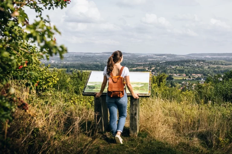 une randonneuse devant une table d'orientation qui admire le paysage