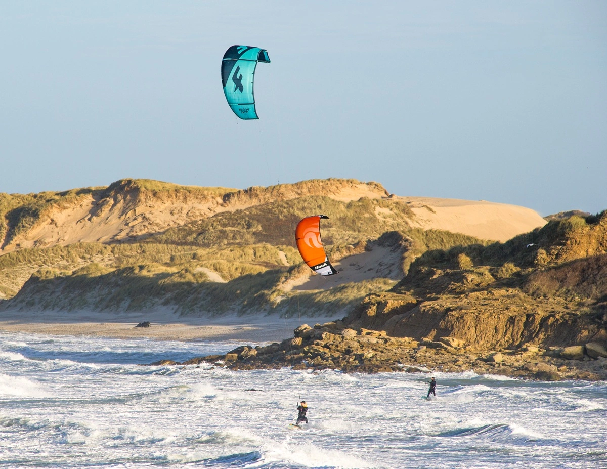 des kite surf sur une mer agitée et des dunes de sables dans le fond