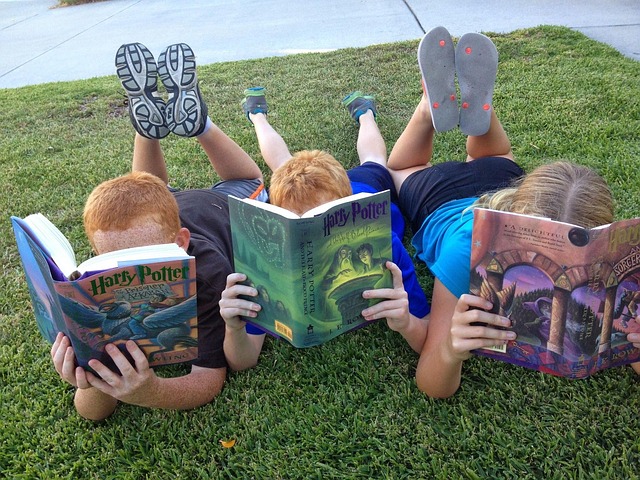 trois enfants allongés dans l'herbe qui lisent un livre