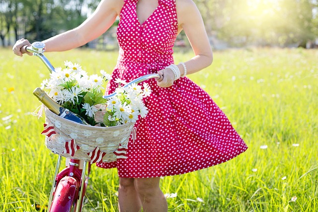 femme avec une obe rouge tenant un velo avec un panier fleuri